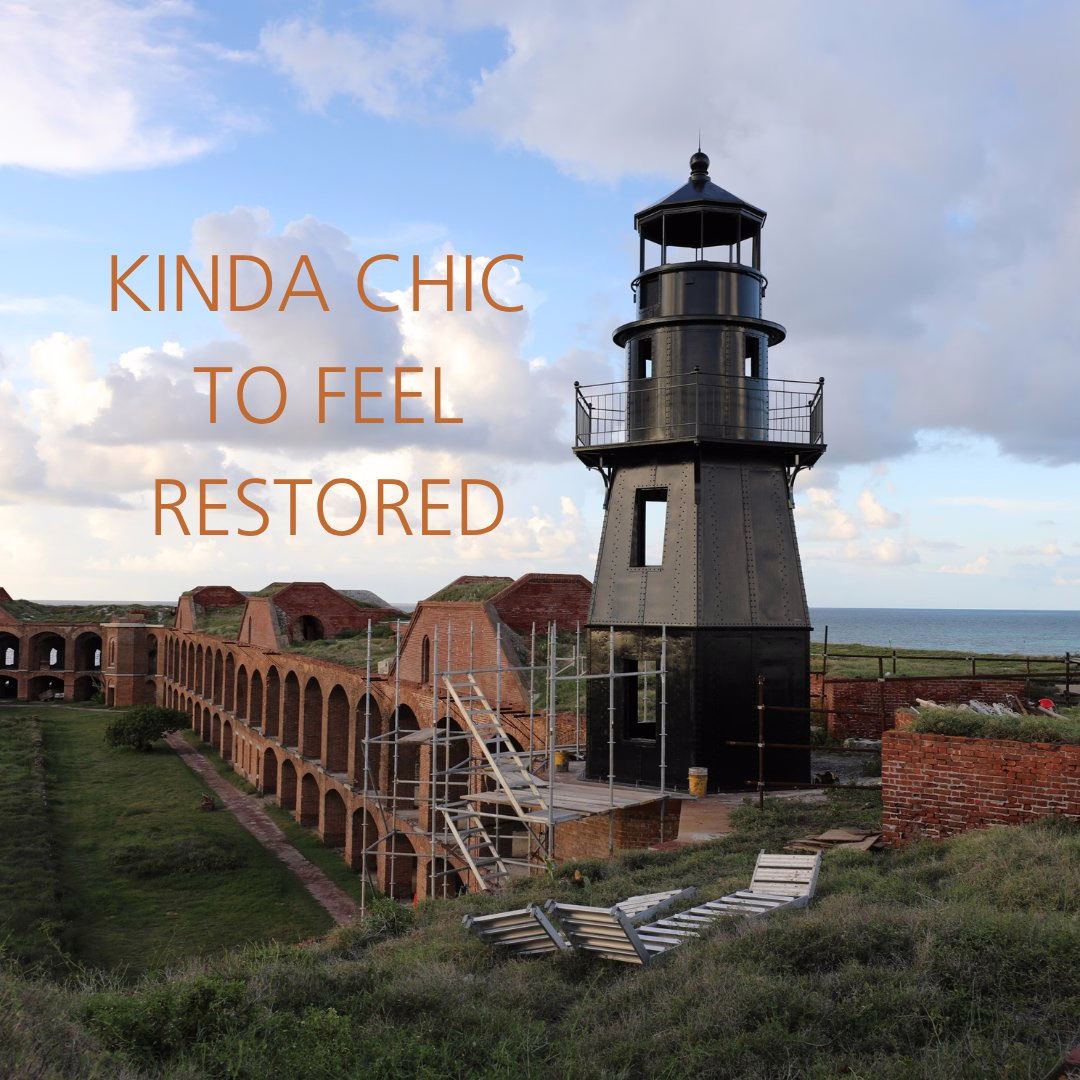 The black Harbor Lighthouse stands atop a bastion of Fort Jefferson with clouds in the background next to the words "kinda chic to feel restored."