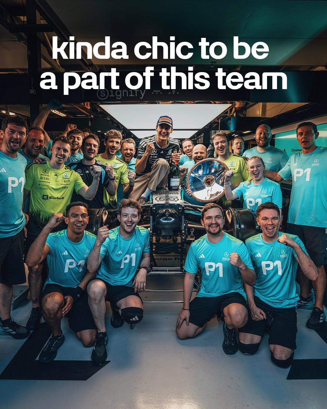 Mercedes mechanics wearing turquoise P1 shirts celebrating in the garage with George after his win in Australia. Above them reads “kinda chic to be a part of this team”
