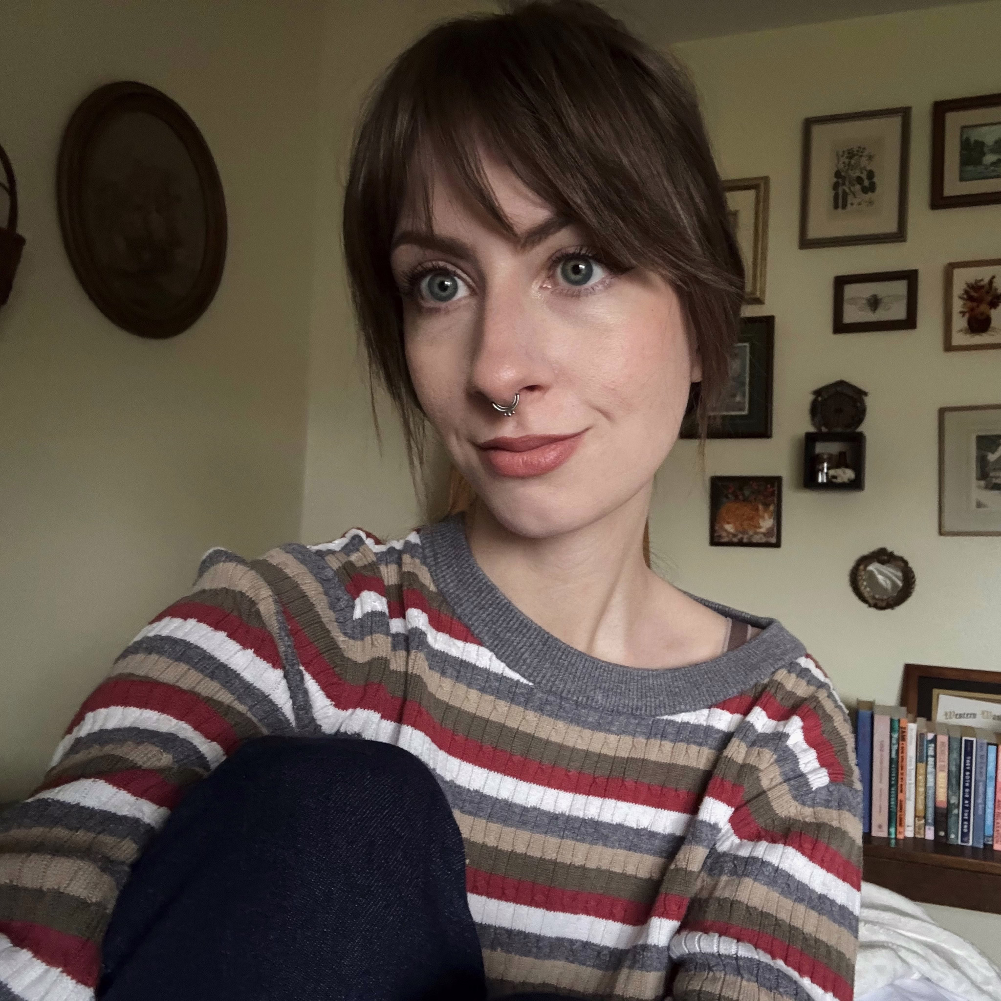 me sitting on my bed. i have my hair pulled back and i’m wearing a striped sweater and jeans
