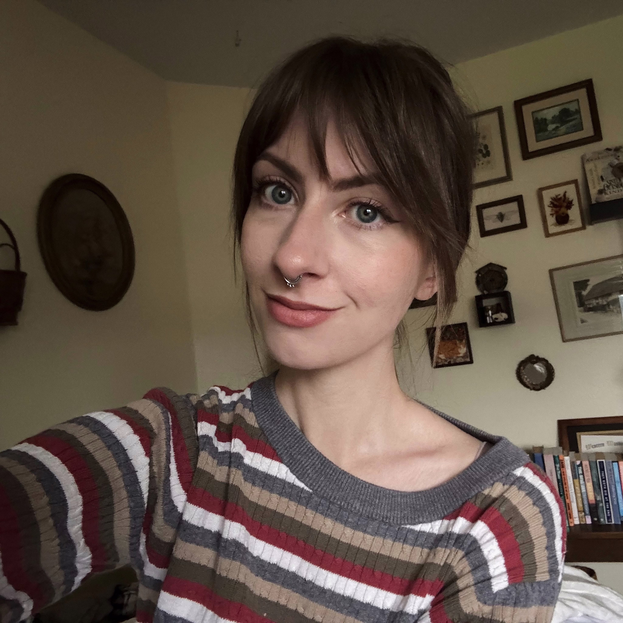 me sitting on my bed. i have my hair pulled back and i’m wearing a striped sweater