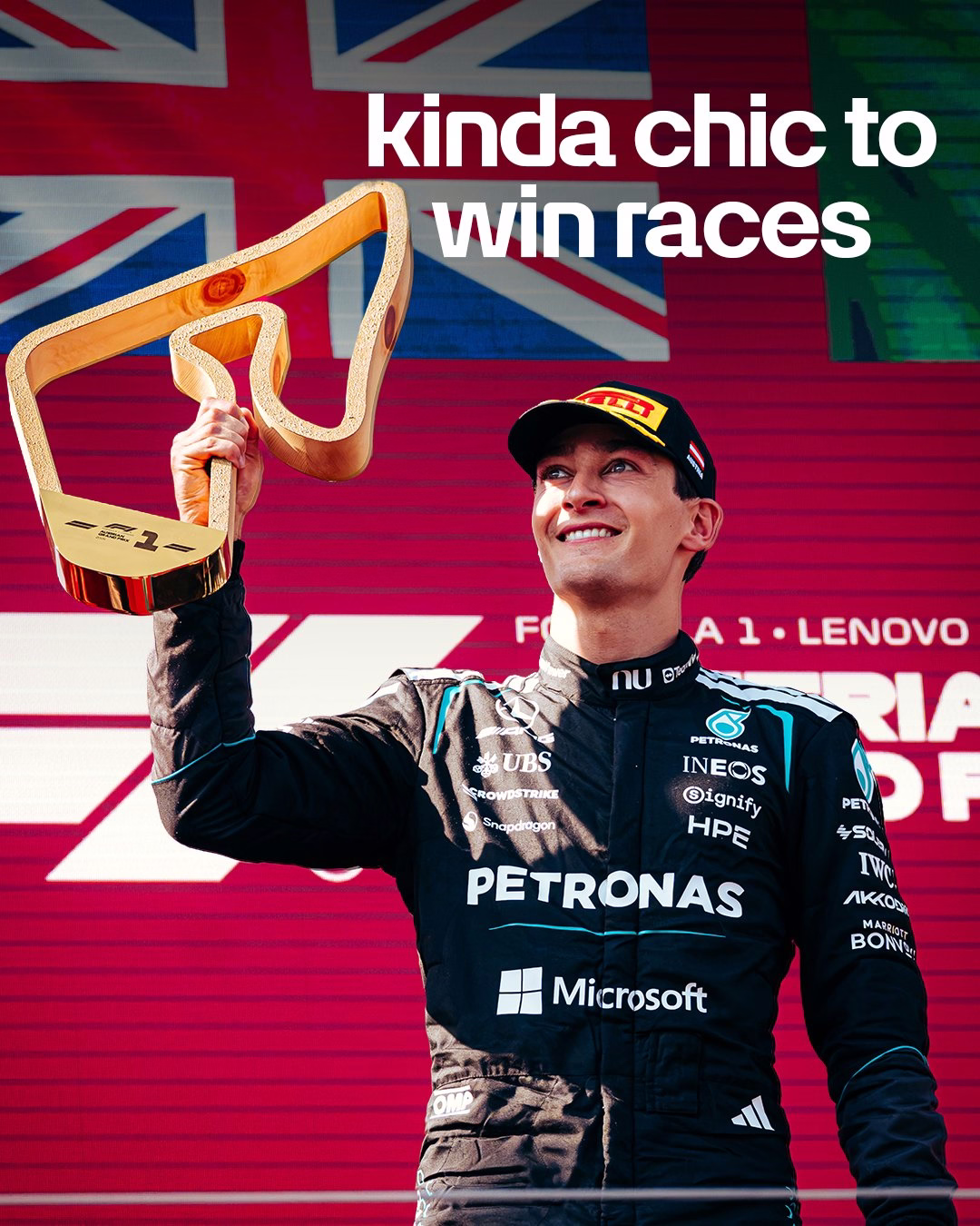 George Russell stood on the podium holding a trophy above his head, wearing a black Mercedes race suit and black Pirelli hat. Above him reads “kinda chic to win races.”