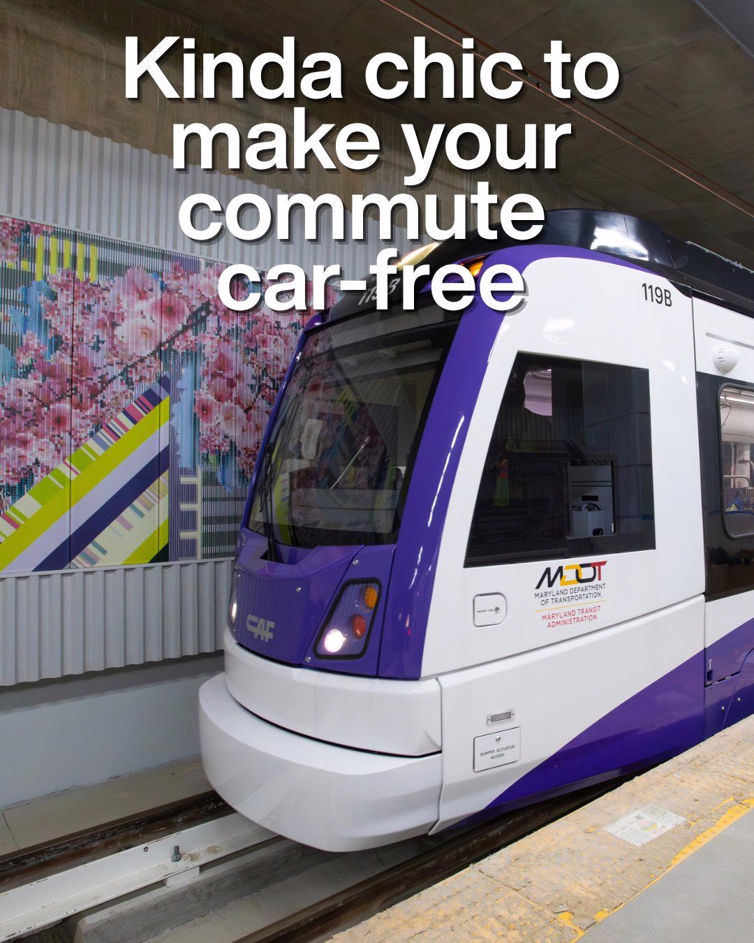 Modern purple and white light rail train at a station platform under an overpass with colorful mural in the background.